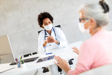 Senior woman with protective facial masks receive news from black female doctor