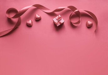 on a pink background lies a red gift with a bow, a satin ribbon and candies in the form of hearts. preparation for the holiday