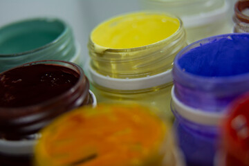 Jars of acrylic paint in red, yellow, purple shades close-up.