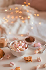 White cup of tasty cocoa drink with marshmallows white background. Decoration garlands of lights. Winter dessert beverage.