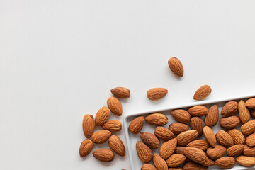 Fresh almonds nuts in flat white plate and scattered on the table