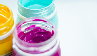 Jars of acrylic paint in blue, yellow, purple shades close-up.
