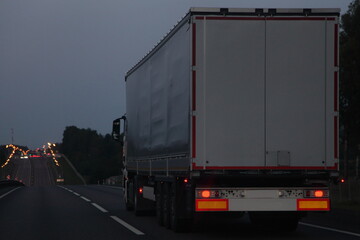 Semi trailer trucks van move on dry asphalted evening road in dusk, back view - intrenational transportation logistics