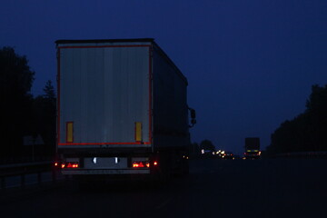 Semi trailer truck move on dry asphalted night road in dark, back view - intrenational transportation logistics