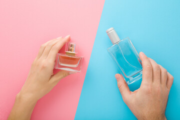 Young adult man and woman hands holding perfume bottles on blue pink table background. Pastel...