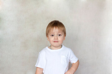 Naklejka premium Portrait of a cute little boy in a white t-shirt. Children's emotions. Child on the background of the wall. Success, bright idea, creative ideas and concepts.
