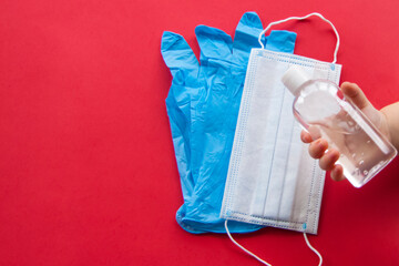 Medical mask with gloves and disinfectant in the child's hand on a red background. Mask for protection against influenza viruses, coronavirus, COVID-19.