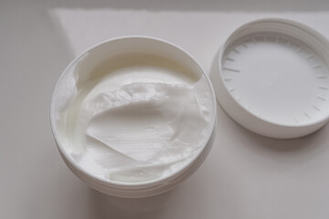 Opened white jar of cosmetic face cream with lid on a black slate background