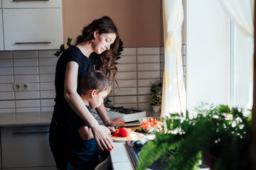 Beautiful mom and son cut fresh vegetables for salad with a knife