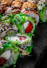 set of sushi roll with salmon, avocado, cream cheese, cucumber, rice, caviar, eel, tuna in plate on black background