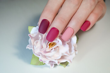 Hand of a young woman with a manicure in pink tones and a flower on a white background.