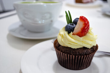 Chocolate cupcake with buttercream, blueberries and strawberries on a white plate.