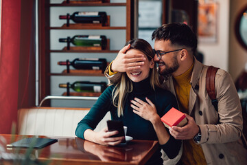 Young man surprising his beautiful girlfriend with a gift box