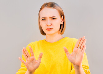 Portrait of a beautiful girl showing stop sign with palms isolated on a gray background