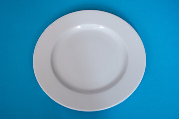 Empty, plain white round plate on a light blue background