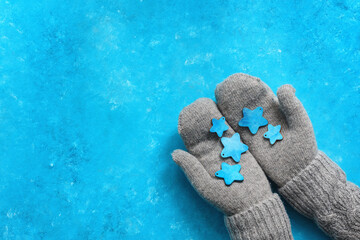 Female hands in mittens and a sweater hold blue wooden stars. Blue grunge background. Christmas greeting card. Top view, flat lay.