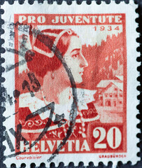 Switzerland - Circa 1934 : a postage stamp printed in the swiss showing a portrait of a woman from Graubünden in historical costume in the background a house