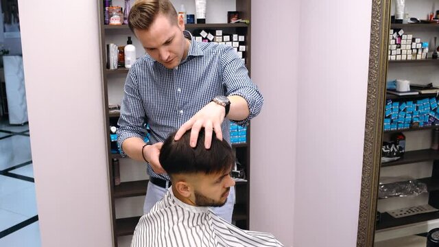 A skilled miller does his job. With the hair clipper he does a young man's hairstyle. He is a miller with a lot of experience and he knows his job well. The customer is satisfied with the result.