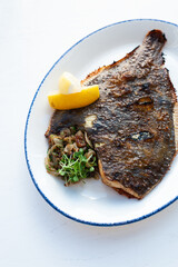 Close up fried flatfish flounder with lemons and crispy crust on a white plate on a white background, top view