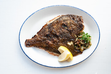 Fried flatfish flounder with lemons and crispy crust on a white plate on a white background, top view