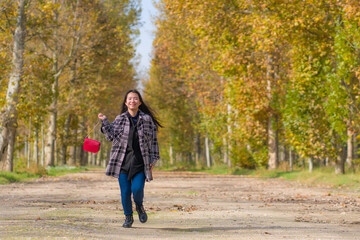 Fototapeta premium outdoors lifestyle portrait of young happy and pretty Asian Chinese woman walking relaxed and cheerful at beautiful city park in vibrant yellow and orange Autumn tree leaves