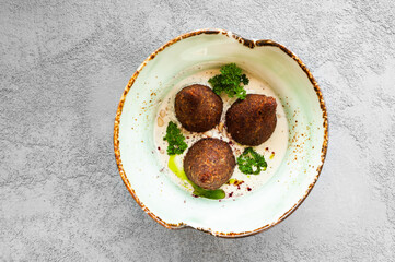 Arabic cuisine meat appetizer kibbeh on a plate. Fried meatballs in yoghurt sauce with pine nuts. Top view