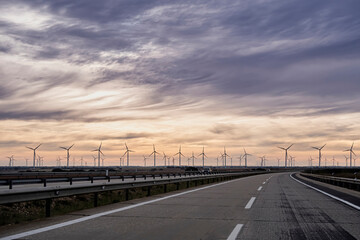 lonely highway at sunrise with a line of windmills on the horizon and soft orange and blue clouds