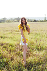 Beautiful woman in yellow dress walks on the field with flowers
