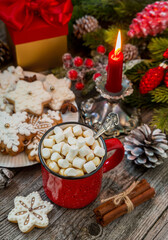 Red mug of coffee with marshmallows and gingerbread on a wooden table against a background of fir branches. Christmas still life.