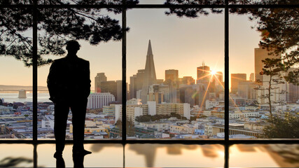 Fototapeta na wymiar silhouette of a man in the window looking at city skyline sunrise