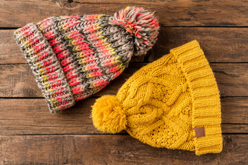 Colourful winter hats with pompons on wooden background. Top view