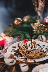 Closeup of a strudel with a strawberry on a Christmas plate near bamboo branch. Christmas breakfast on a wooden table.