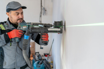 an electrician makes a recess in the wall for a socket in the place marked with a laser pointer.