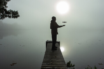 Man playing with the drone. Silhouette against the foggy landscape.Male operating the drone by...