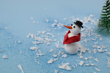 Snowman with a hat and a scarf with paper snow and tree on blue background