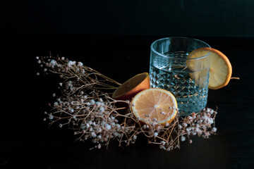 Alcohol drink (gin and tonic cocktail) garnished with lemon fruit and flower isolated on black background. Iced cocktail drink with lemon and herbs.