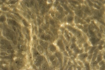 Ripples on the water, sea water near the coast, sand is visible through the water, top view