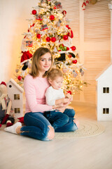Cute little boy with blond hair plays with his mother in a bright room decorated with Christmas garlands near the Christmas tree. Happy childhood. Christmas mood