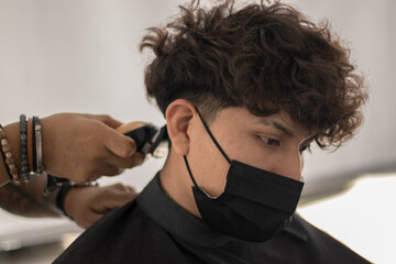 Session in a hair salon with a young hairdresser with a mask cutting the hair of a boy with a mask in times of pandemic