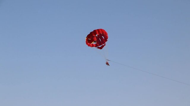 Couple parasailing on red parachute in the sky