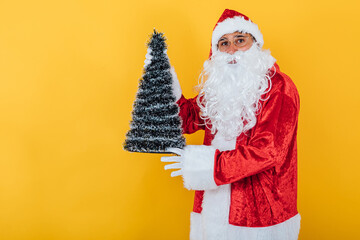 Santa Claus holding a Christmas tree on yellow background. Christmas concept