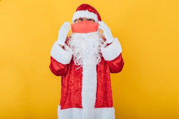 Santa Claus putting on a red face mask, on yellow background. Christmas concept