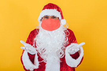 Santa Claus wearing a red face mask with a gesture of resignation, on a yellow background. Christmas concept