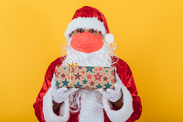 Santa Claus wearing a red face mask and holding a gift, on yellow background. Christmas concept