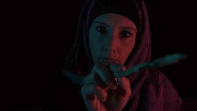 A night portrait of a witch casting spell and making witchcraft with a magic wand, she is looking at a camera