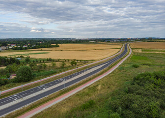 Fototapeta na wymiar Aerial view of Long highway between yellow wheat fields at cloudy day