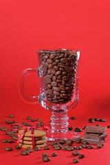 Grain coffee in glass cup with chocolate bar and cookies on red background