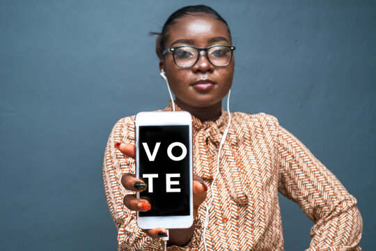 Closeup shot of a young lady wearing headphones holding her phone with writing "Vote"