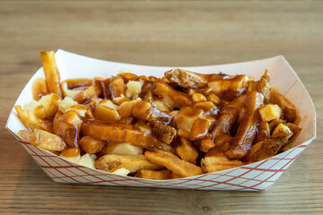 a takeaway paper box of poutine with french fries, cheese curds and gravy