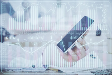 Double exposure of man's hands holding and using a digital device and forex graph drawing. Financial market concept.